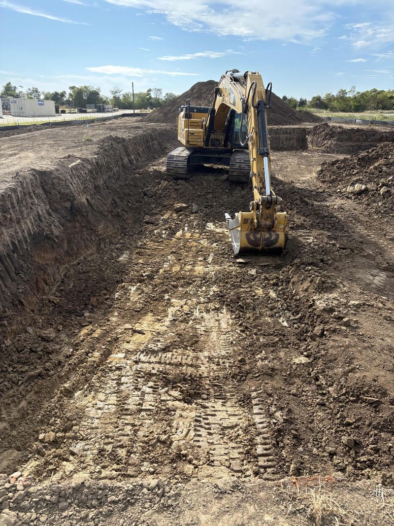 Excavator working in a long, deep cut with straight dirt walls