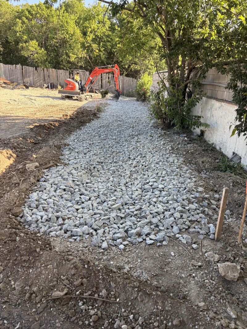 Crushed rock base placed alongside a building, with a mini excavator working behind