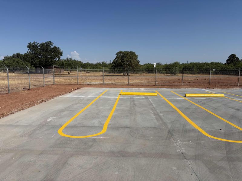 Concrete paving with yellow parking lot striping and parking blocks by Circle H Civil