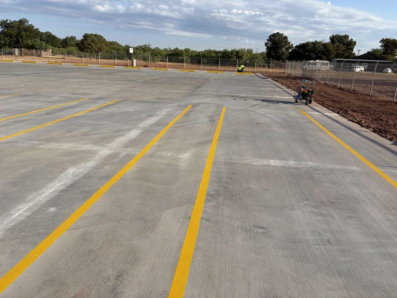 Concrete paving and yellow parking lot striping by Circle H Civil, beside a red-dirt edge