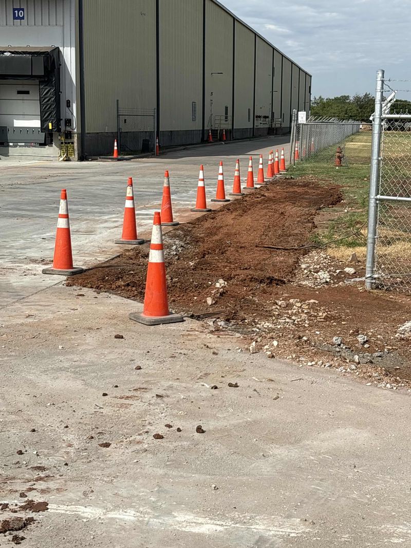 Utility trench dug along a warehouse, lined with orange cones